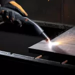 A worker manually cutting a metal block using a plasma cutter