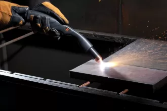 A worker manually cutting a metal block using a plasma cutter